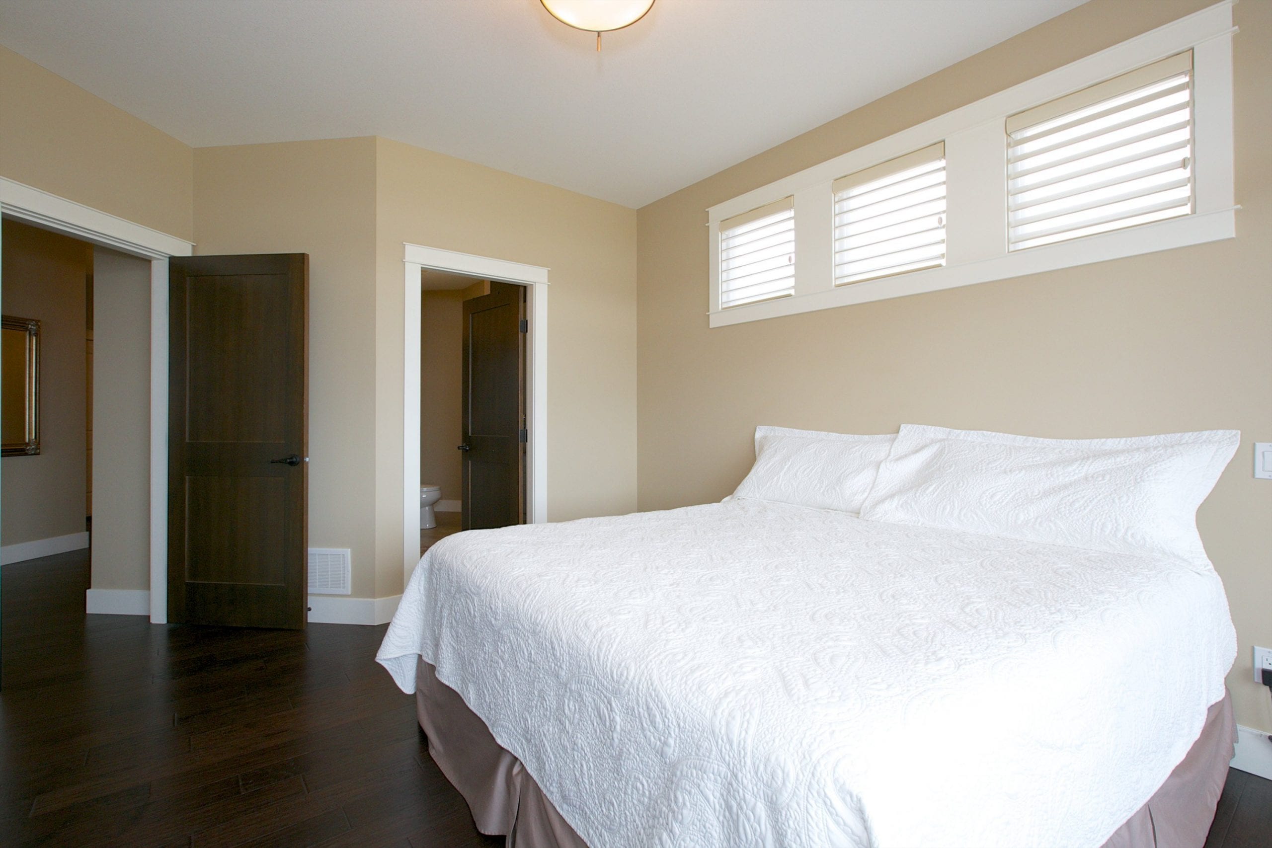 interior shot of west harbour home master bedroom with three windows directly above the bed and two doors in view