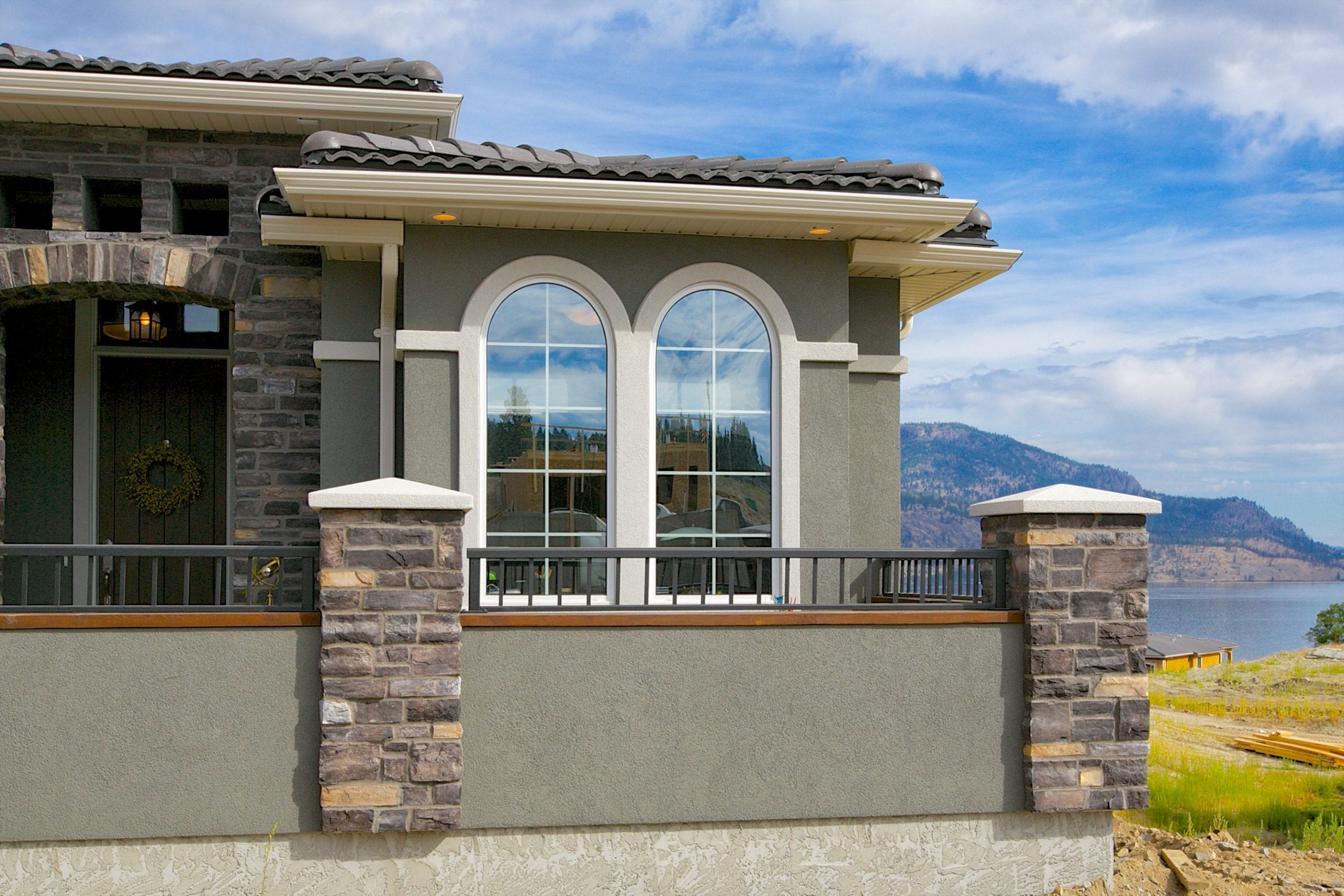 exterior shot of sage coloured west harbour home with mountains and the okanagan lake in the background