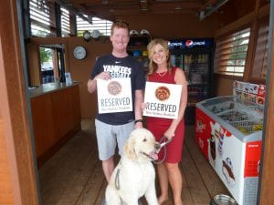 couple holding up reserved signs with west harbour logo on them while also holding a dog on a leash