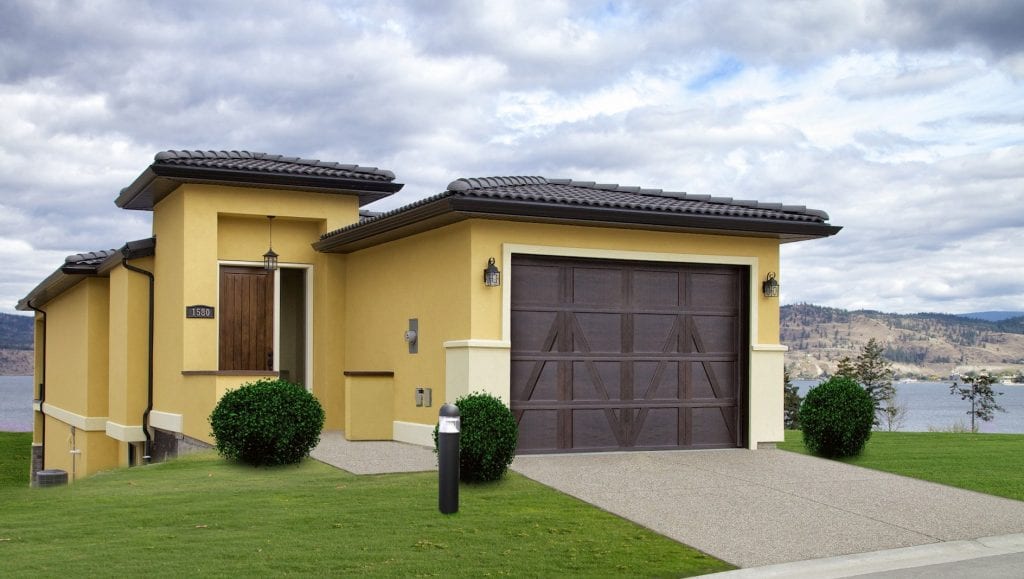 exterior shot of dandelion coloured west harbour home with landscaped grass in foreground and okanagan lake in background