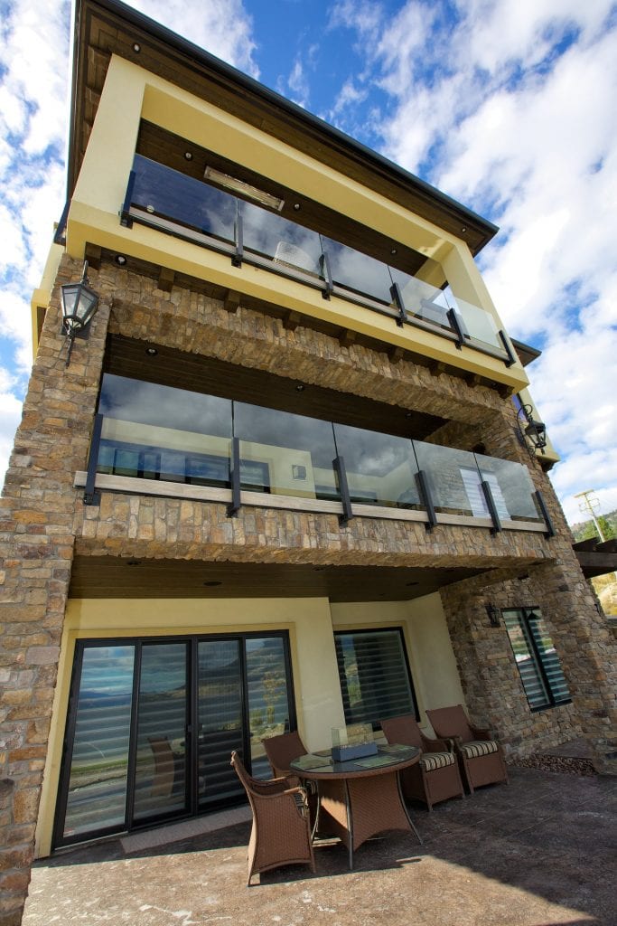 upwards looking shot at exterior of tan and stone west harbour home with chairs and tables arranged along the outside of it