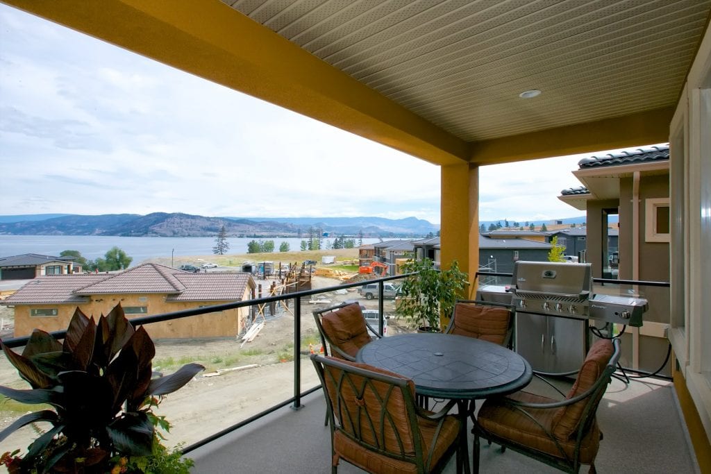 patio shot overlooking lake with three chairs a table a houseplant and a grill