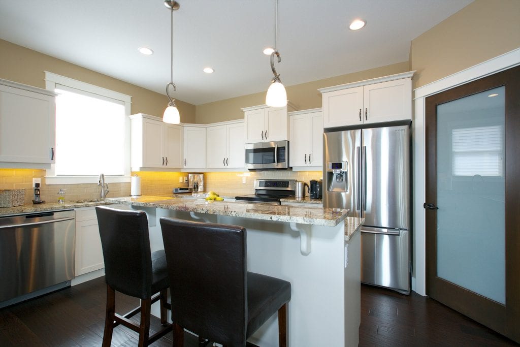 interior shot of west harbour home kitchen with white cabinetry bar chairs fridge microwave and stove bar area with chairs