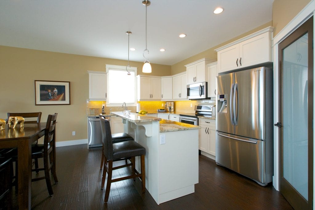 interior shot of west harbour home kitchen with white cabinetry bar chairs fridge microwave and stove bar area with chairs