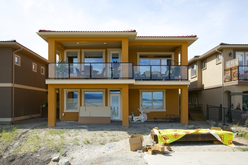 exterior shot of butterscotch coloured west harbour home with a red roof facing a patio with houseplants chairs and tables