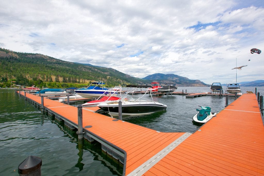 red blue and black boats and a green jet ski docked at west harbour marina amidst a cloudy day